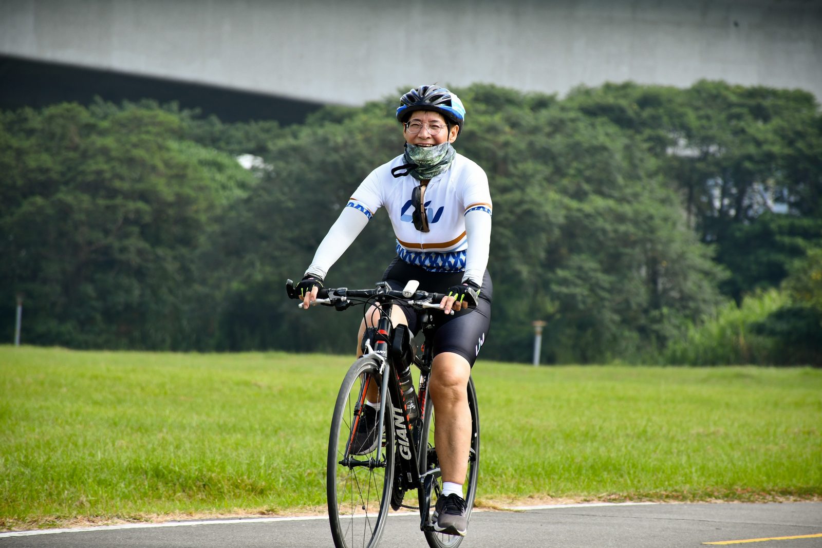A rider smiling behind a bandana, park path beneath a bridge