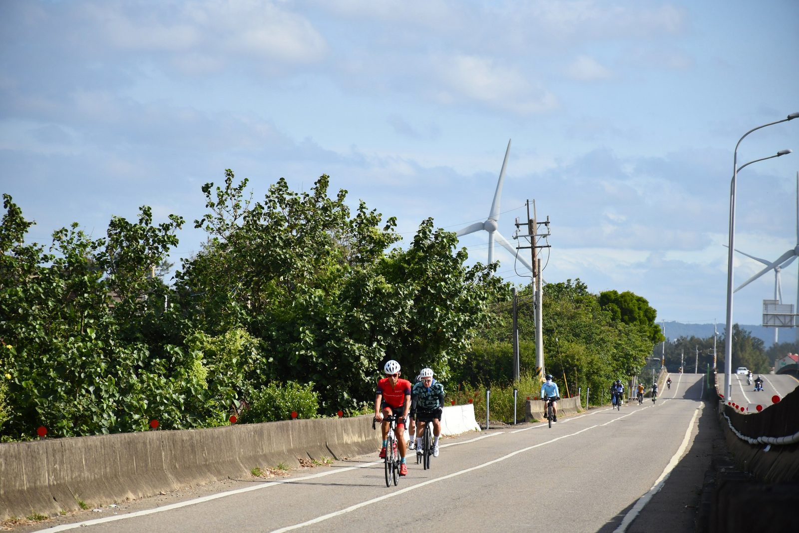 Riders passing a wind turbine along the road