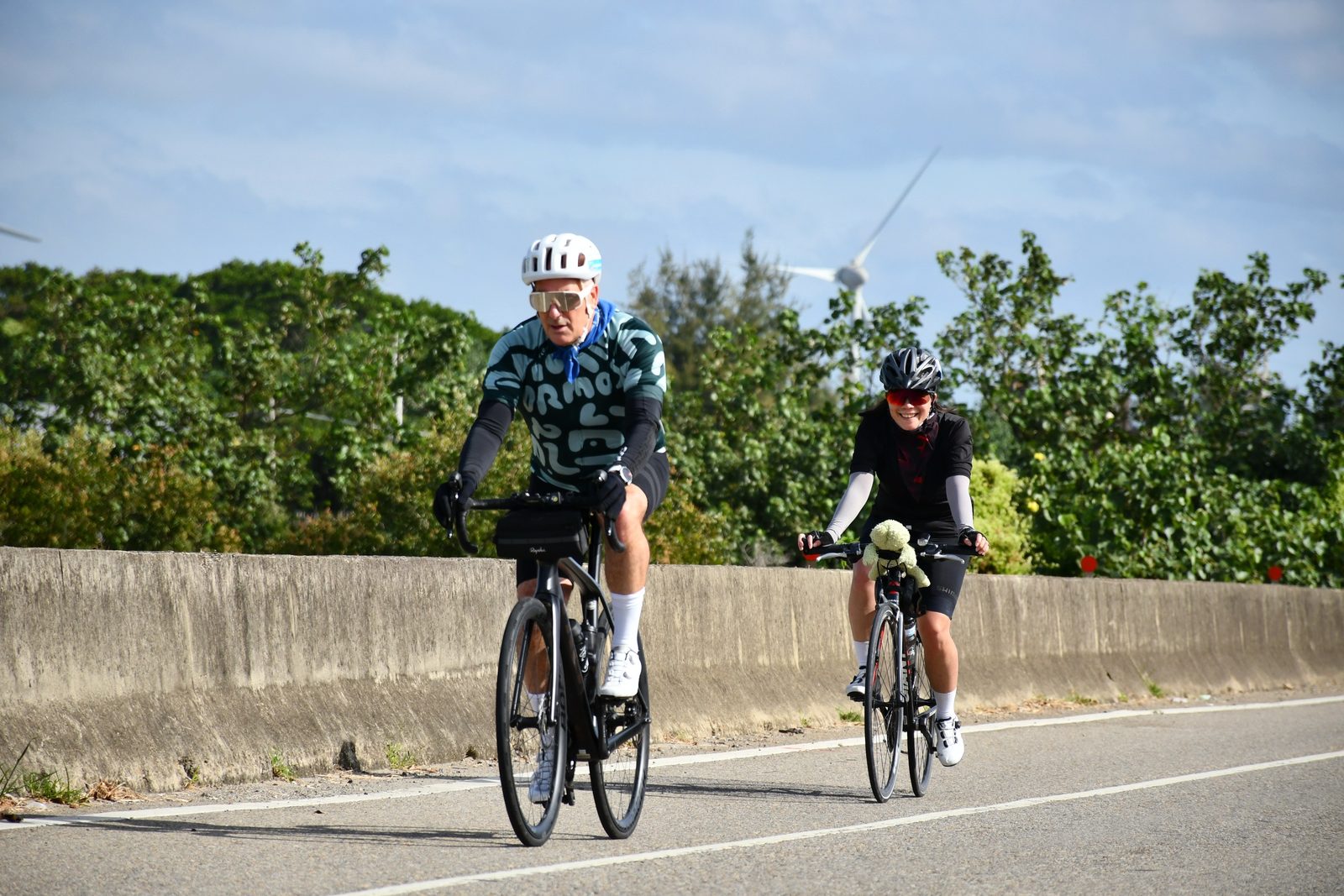 Two riders on the road, a plush mascot along for the ride