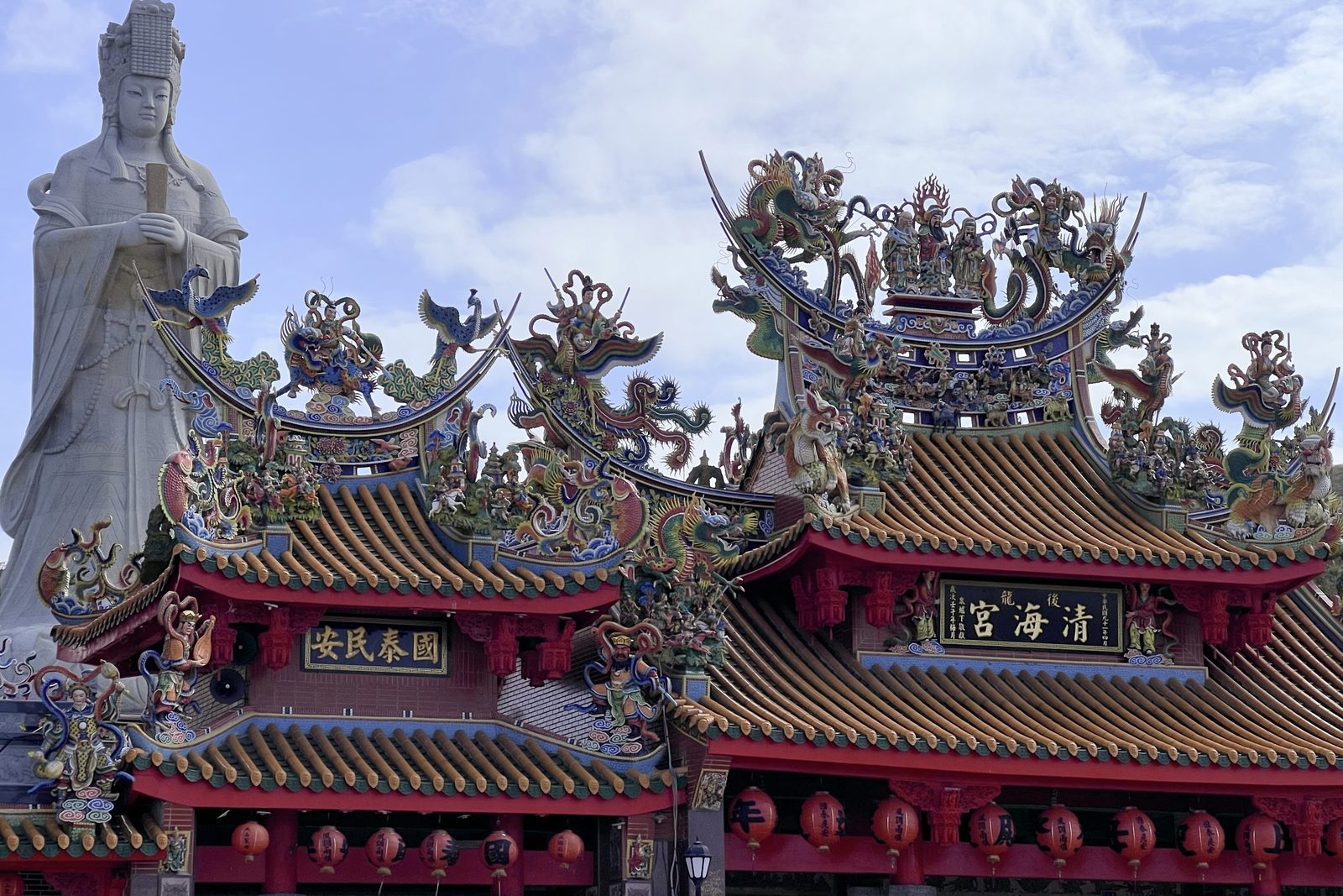 An ornate temple roofline with a towering Guanyin statue behind