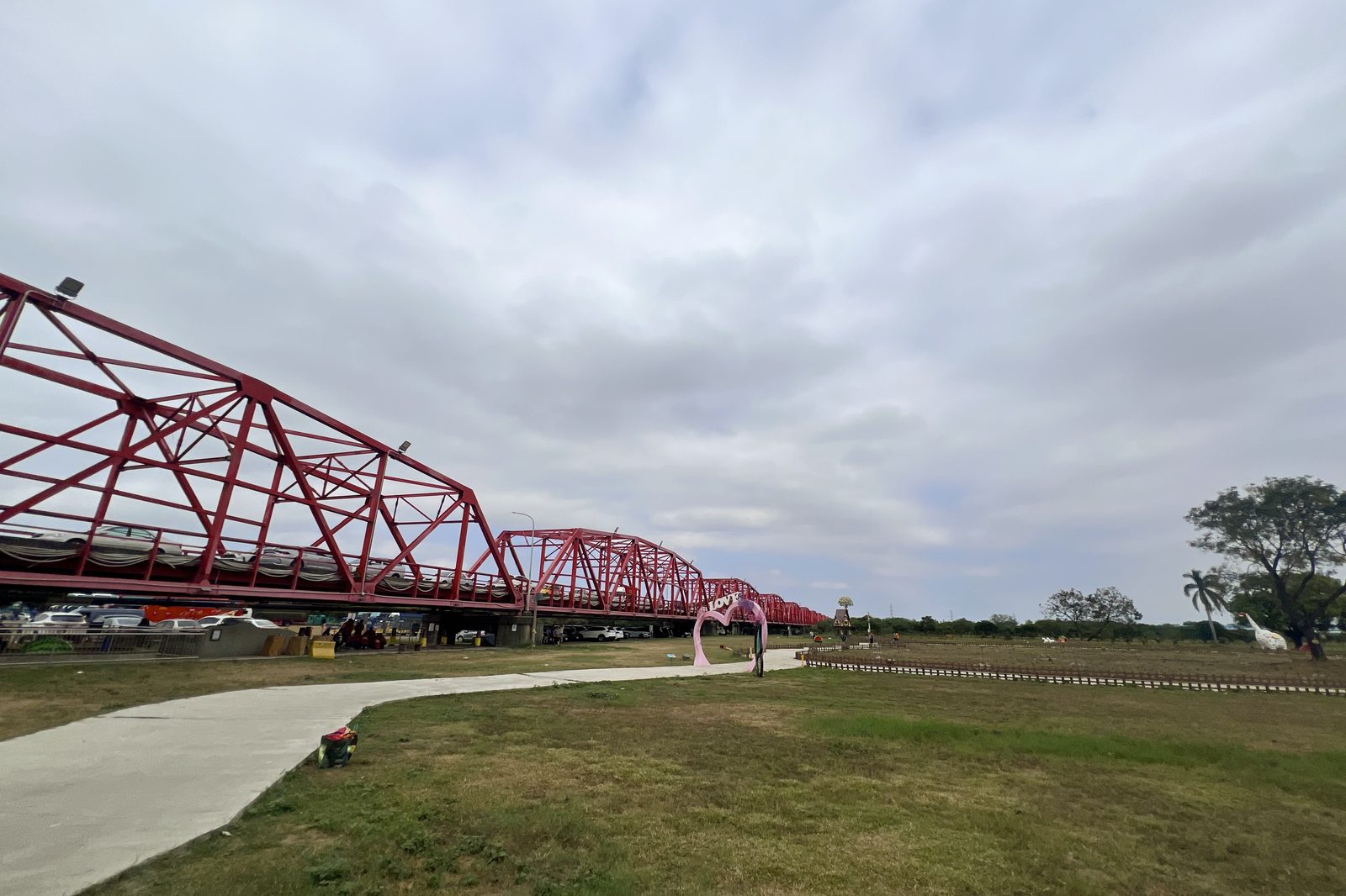 A wide view of the red truss bridge and riverside park