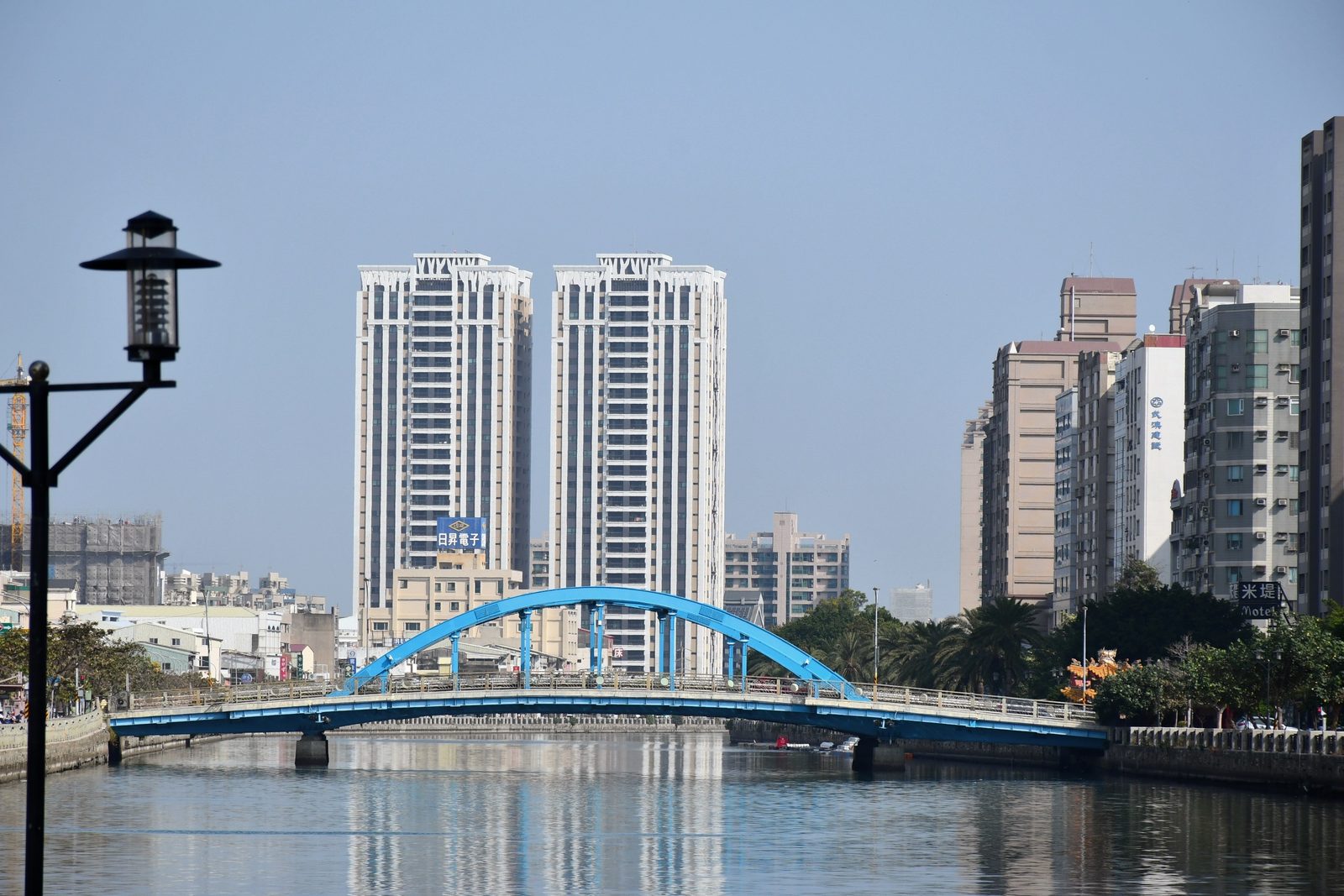A blue arch bridge over the river, towers behind