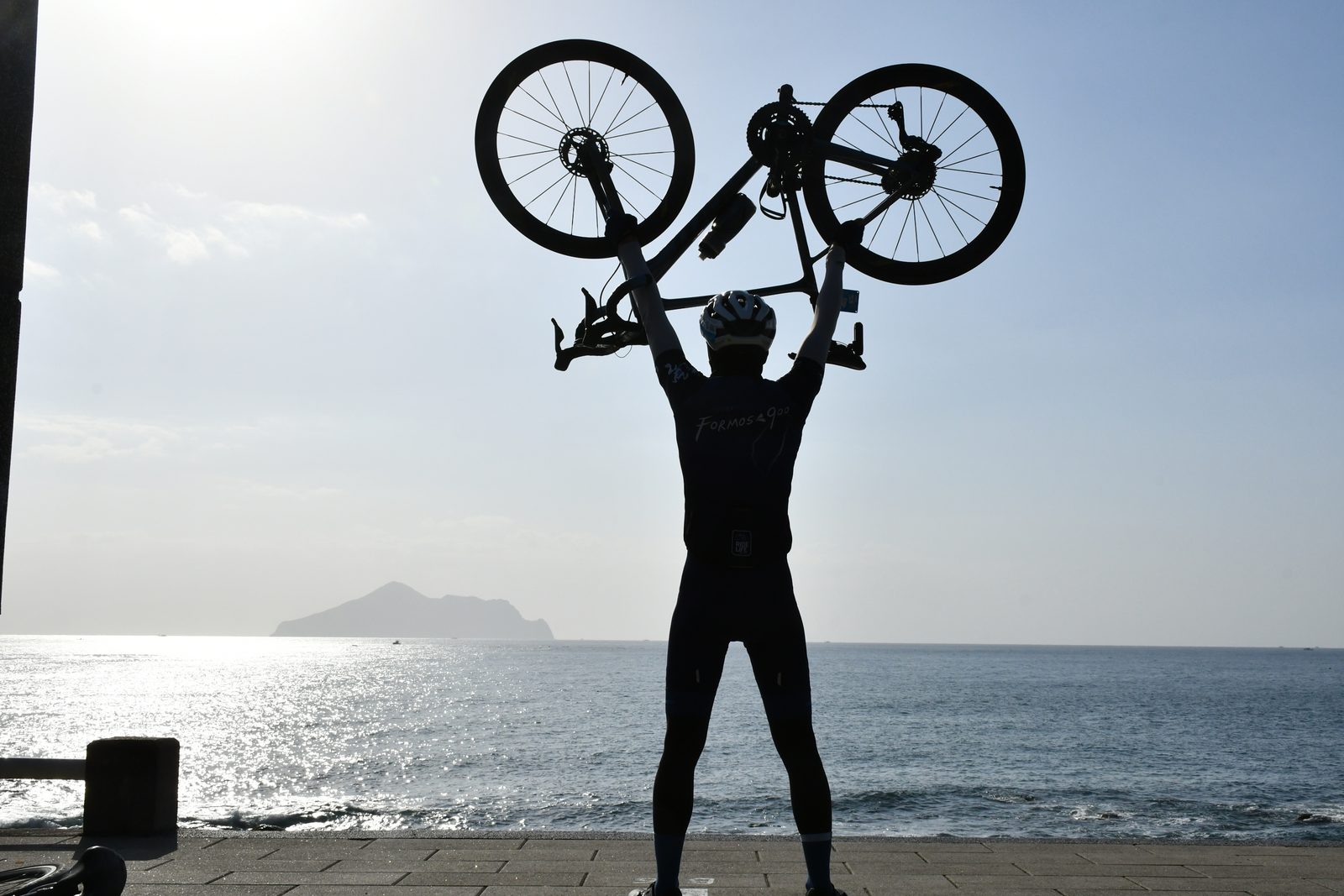 A bike held high in silhouette against the sea